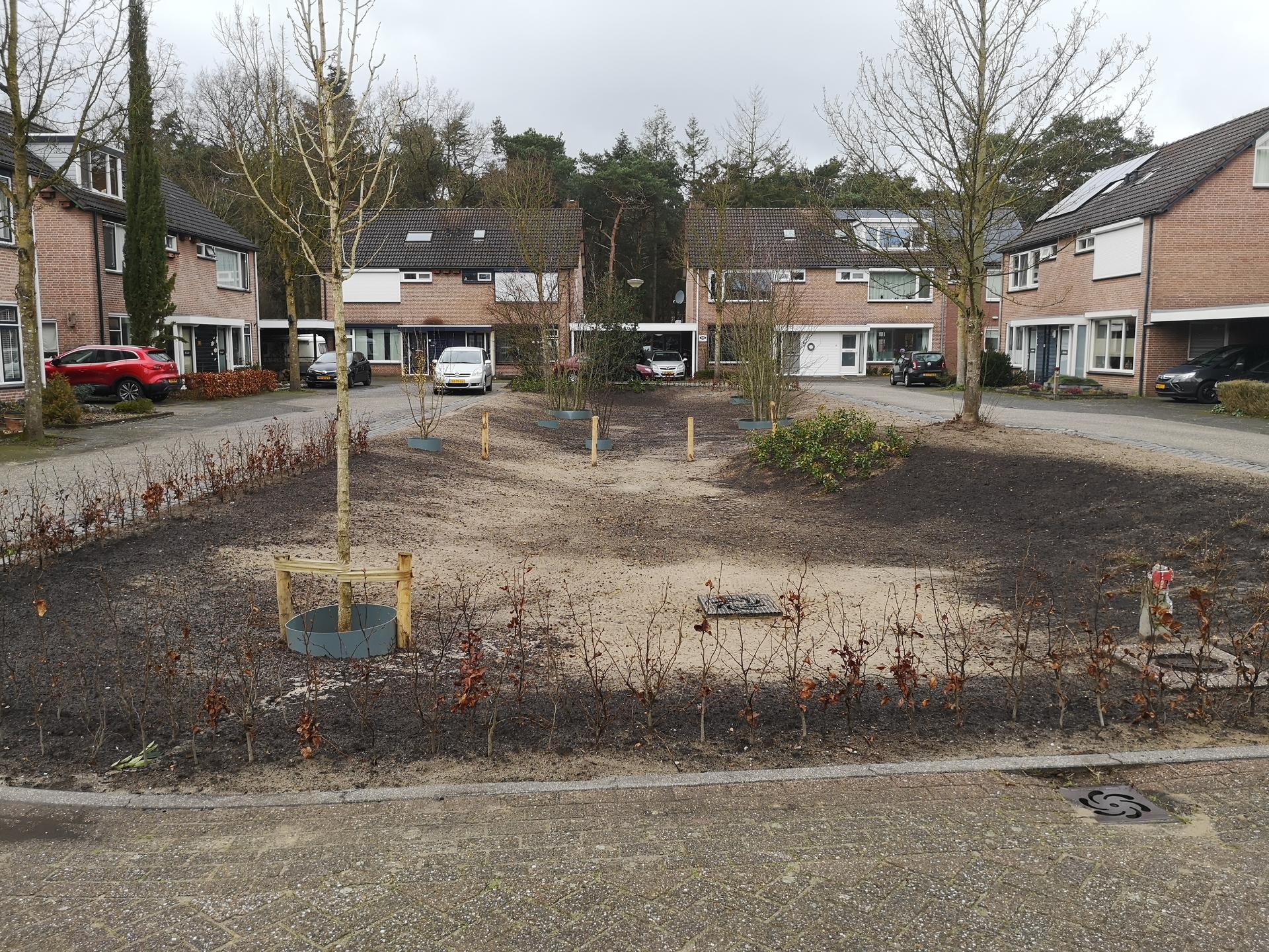 huizen rondom een perkje met zand en bomen
