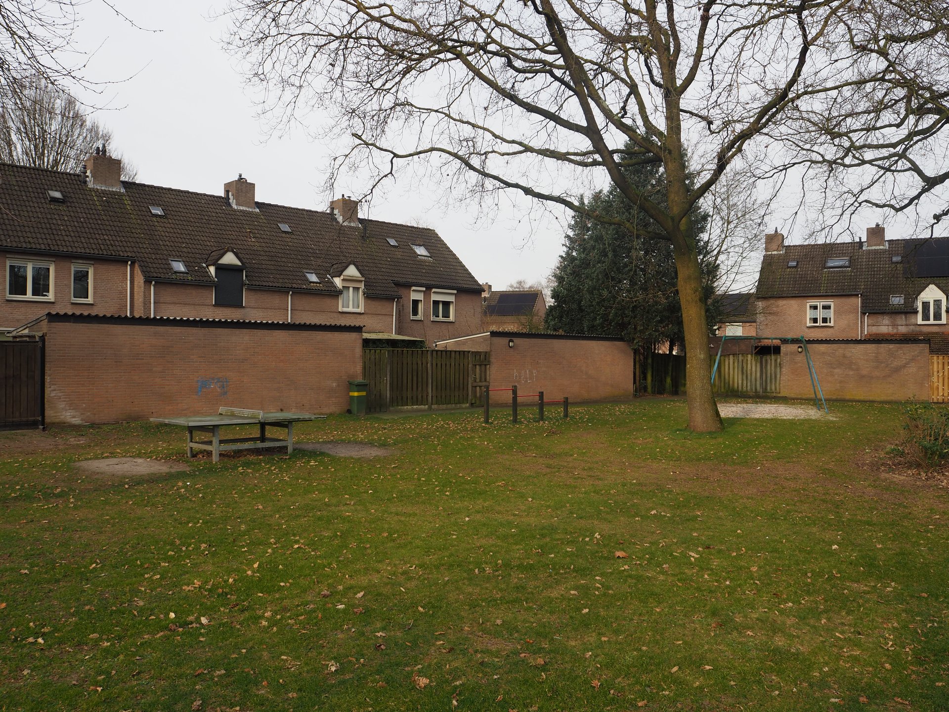 Vergroot afbeelding: aan de linkerkant een tafeltennistafel, rechts daarvan een duikelrek en schommel. Op de achtergrond staan woningen