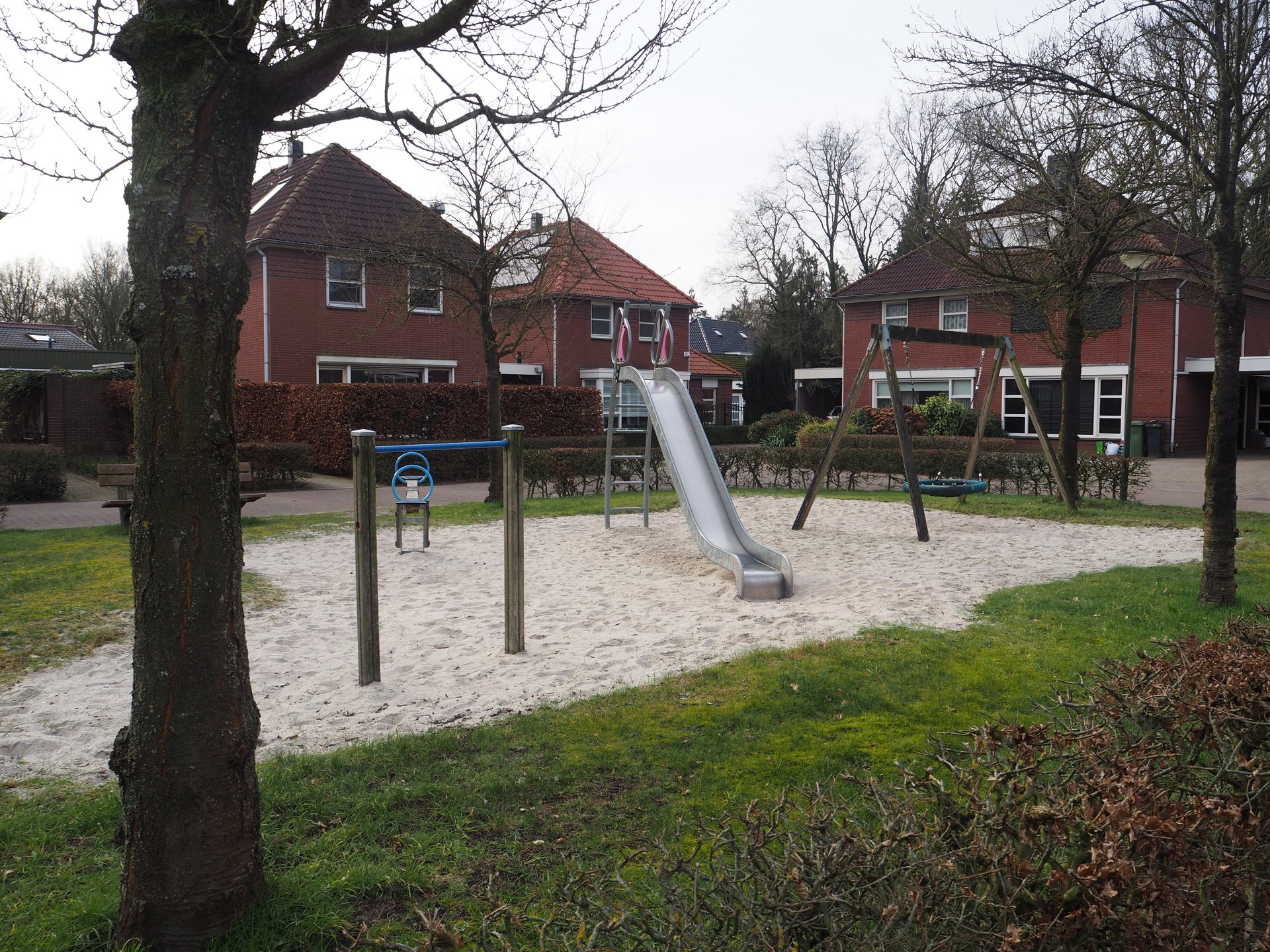 Vergroot afbeelding: aan de linkerkant een duikelrek en wipwap, rechts daarvan staat een glijbaan en daarnaast een schommel. Op de achtergrond staan woningen. 