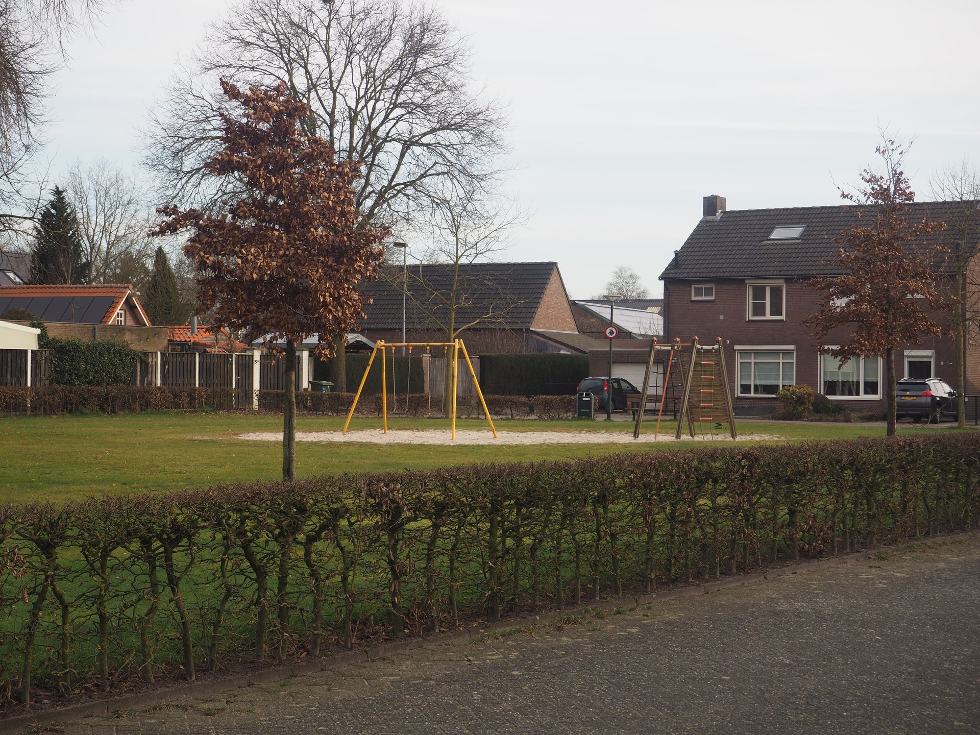 Vergroot afbeelding: een heg met daarachter een schommel en klimrek. Op de achtergrond staan woningen.