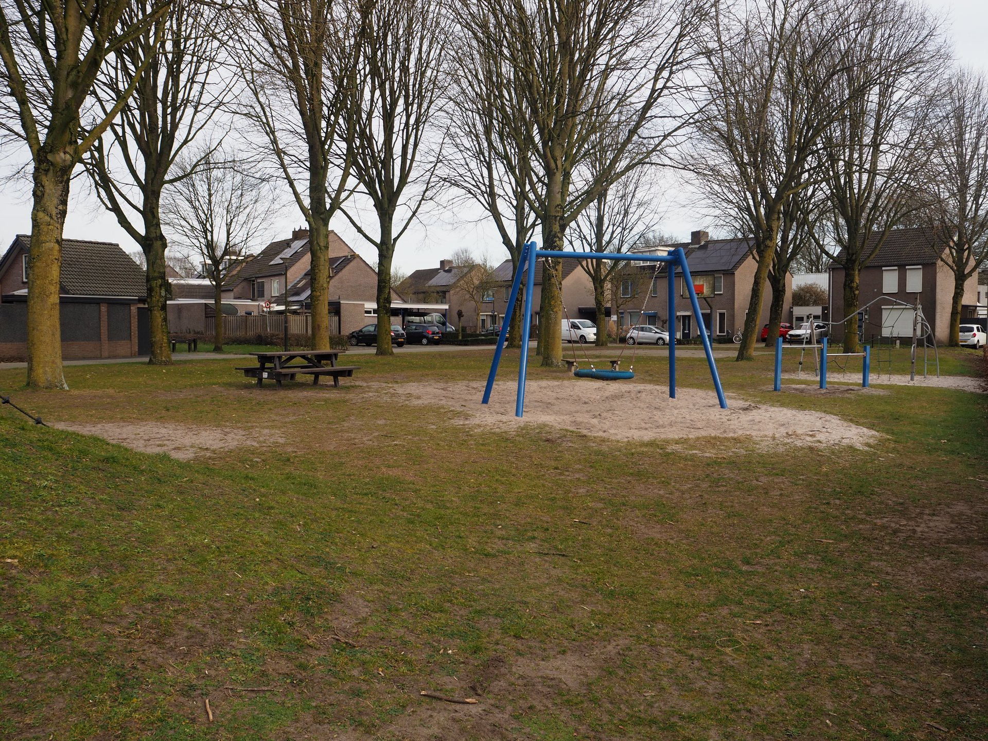 Vergroot afbeelding: aan de linkerkant een picknickbank met daarnaast een schommel en duikelrek met op de achtergrond woningen