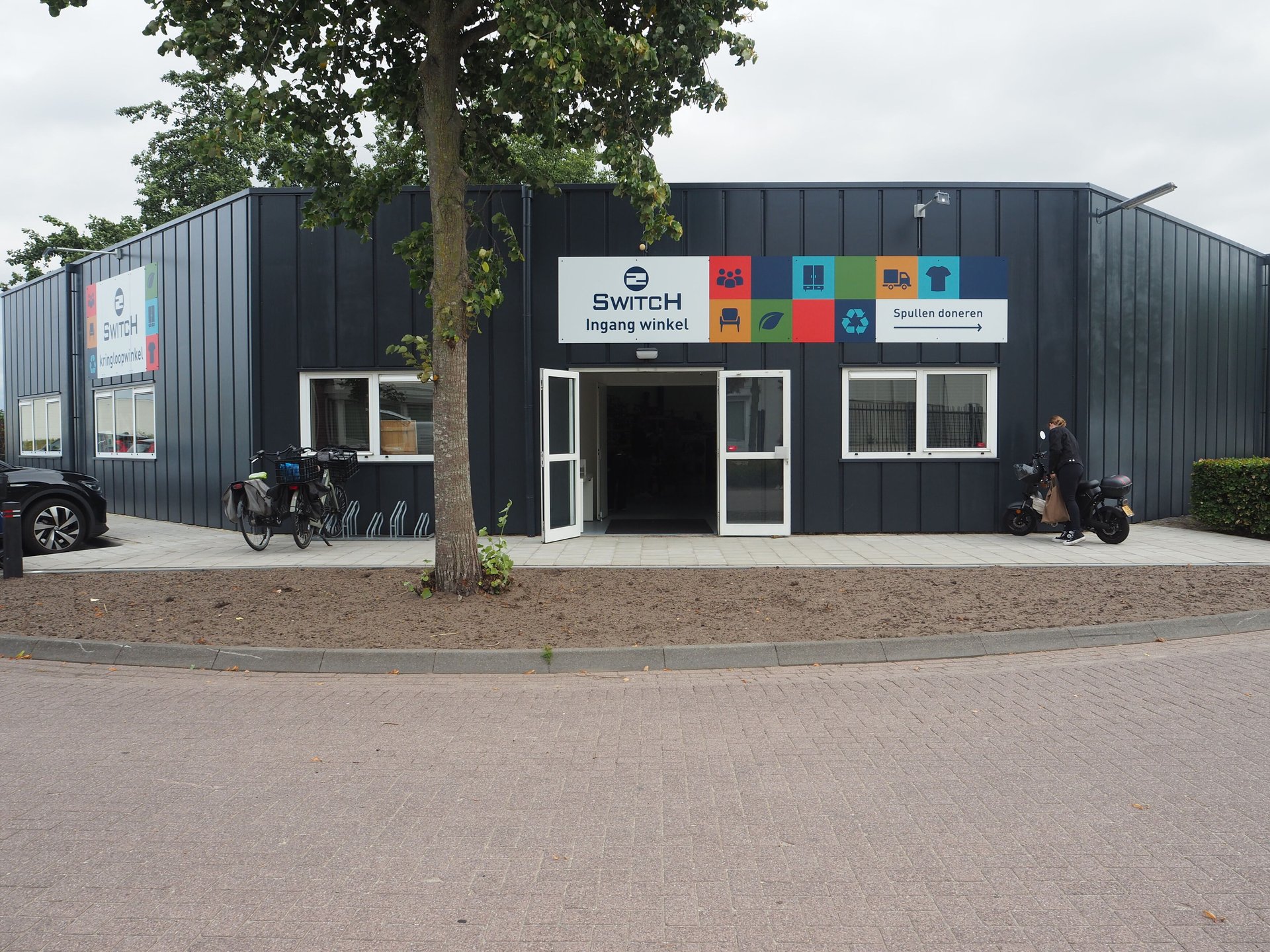 Vergroot afbeelding: het pand van de kringloopwinkel met daarvoor een boom.