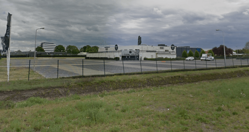 Vergroot afbeelding: het pand van Time Out met daarvoor de parkeerplaats, een hek en de berm