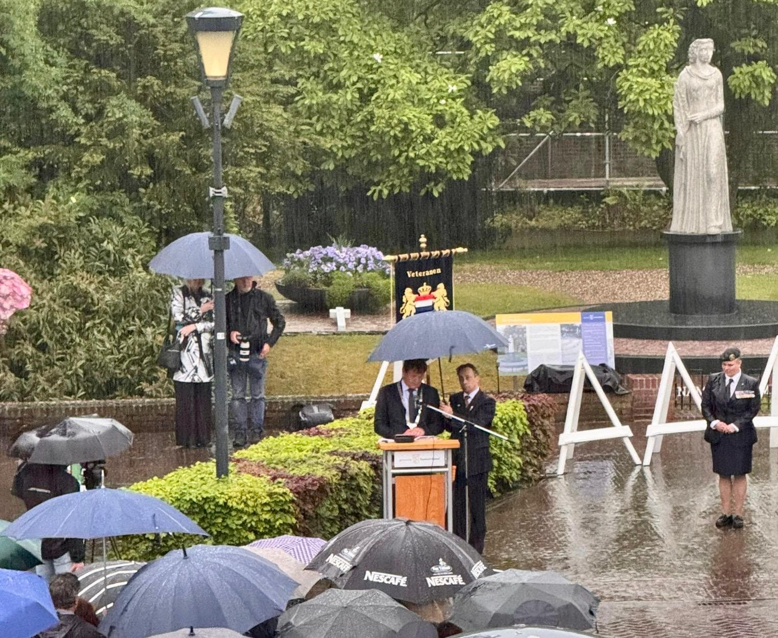 Vergroot afbeelding: burgemeester Michiel van Veen spreekt de aanwezigen toe. Naast de burgemeester staat een persoon die een paraplu boven hem houdt.Op de achtergrond, rechts van hem, is een standbeeld te zien.
