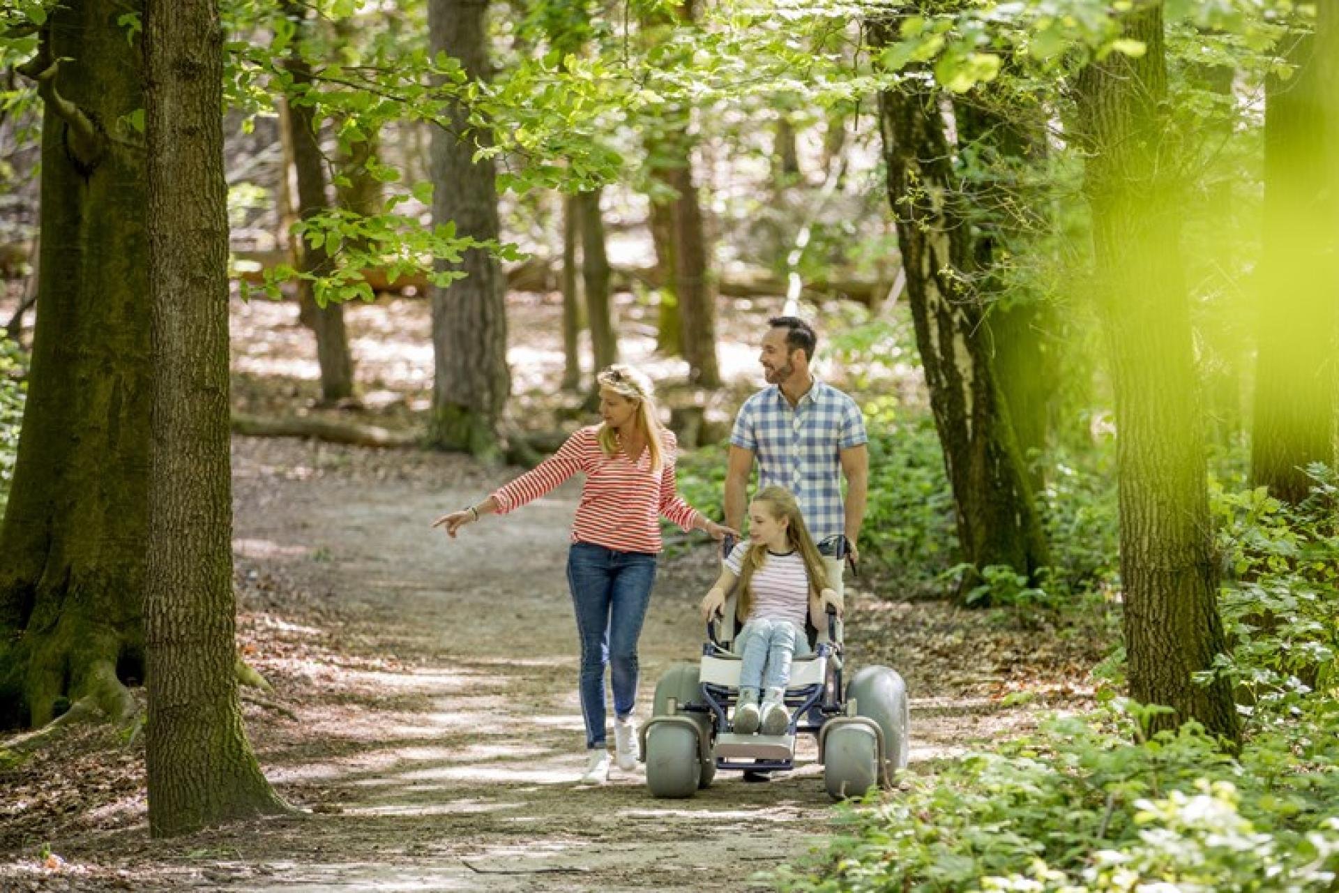 Vader en moeder met kind in een rolstoel die door het bos wandelen